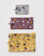 Three recycled nylon zip pouches with hanging loops. The top pouch is light gray with a floral print, the middle pouch is mauve with a floral print, and the bottom pouch is mustard yellow with a floral print.