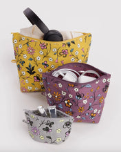 Three floral zippered pouches in yellow, mauve, and gray, each shown open with different accessories inside