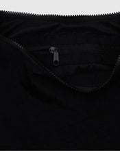 Close-up of a black zippered pocket with a black zipper pull on a black fabric garment, against a light gray background.
