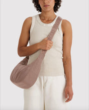 A model wearing a light beige shoulder bag with a wide strap featuring the brand name 'BAGGU' in tonal lettering