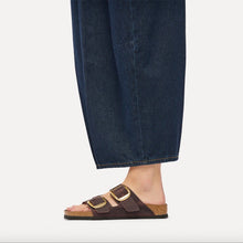A person wearing dark brown double-strap slide sandals with gold buckles, styled with dark blue jeans 
