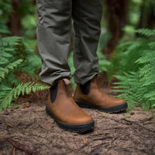 A person wearing olive green pants and brown leather Chelsea boots