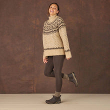 A woman wearing a beige sweater, dark brown leggings, and with dark brown slip-on boots