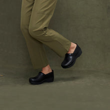 Person wearing black clogs styled with green pants 