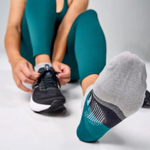 Person wearing green leggings and gray socks with black soles, tying a black athletic shoe