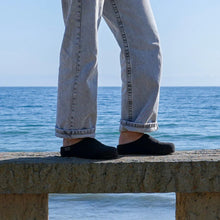 A person wearing light-wash denim jeans and black slip-on clogs