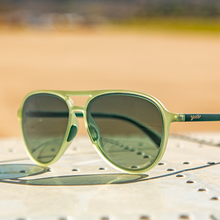 Green sunglasses with dark lenses on a textured surface with a blurred natural background