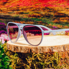 Sunglasses with pink lenses on a wooden stump with a colorful floral background
