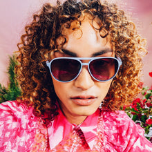 Person wearing sunglasses and a pink floral shirt with a blurred background