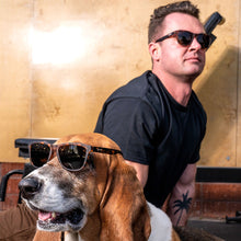 Man and dog wearing sunglasses in front of a gold-colored wall