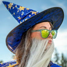 Person wearing a blue wizard hat with stars and sunglasses against a blurred natural background