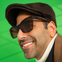 Man wearing a brown cap and sunglasses with a green background