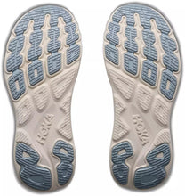 A pair of Hoka shoe soles shown from the bottom, featuring a light beige midsole with textured light blue and gray outsole tread patterns.
