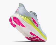A Hoka running shoe in light blue with a thick white midsole, bright neon yellow accents, and hot pink details on the logo and outsole