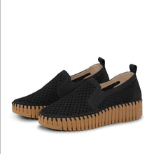 A pair of women's black slip-on platform sneakers in black with a thick, ribbed tan wedge sole