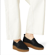 Black knit slip-on platform shoes with brown ridged soles, styled with white wide-leg jeans