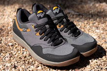 Gray and black sneakers with brown soles on a gravel surface