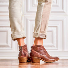 A person wearing brown leather ankle boots styled with light beige rolled-up pants